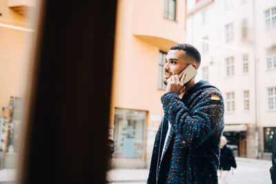 Young businessman talking on smart phone seen through window