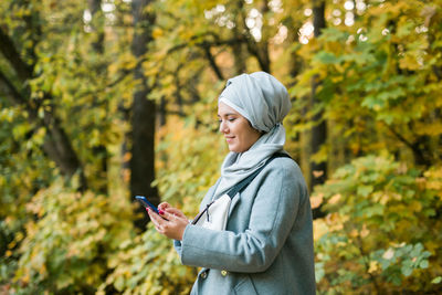 Young smiling woman using mobile phone in forest