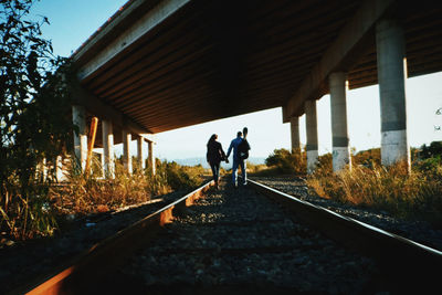 People holding hands while walking on railroad track