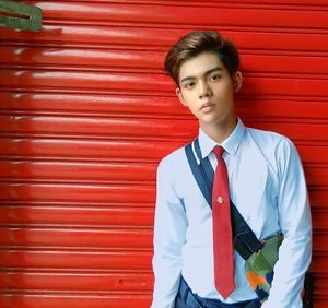 Portrait of young man standing against red wall