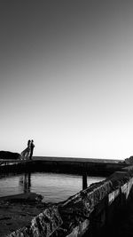 People standing by sea against clear sky