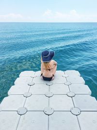 Rear view of woman sitting by sea on pier