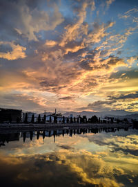Scenic view of river by buildings against sky during sunset