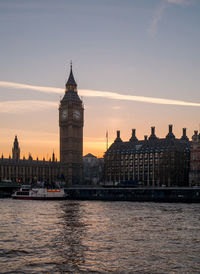 River and buildings against sky during sunset