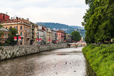 Buildings by river in town against sky