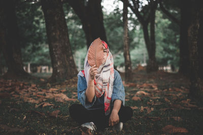 Full length of boy sitting on land in forest