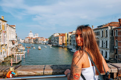 Woman standing on canal in city against sky