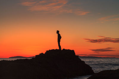 Silhouette man standing on rock against sea during sunset