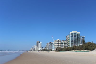 Buildings by sea against clear blue sky