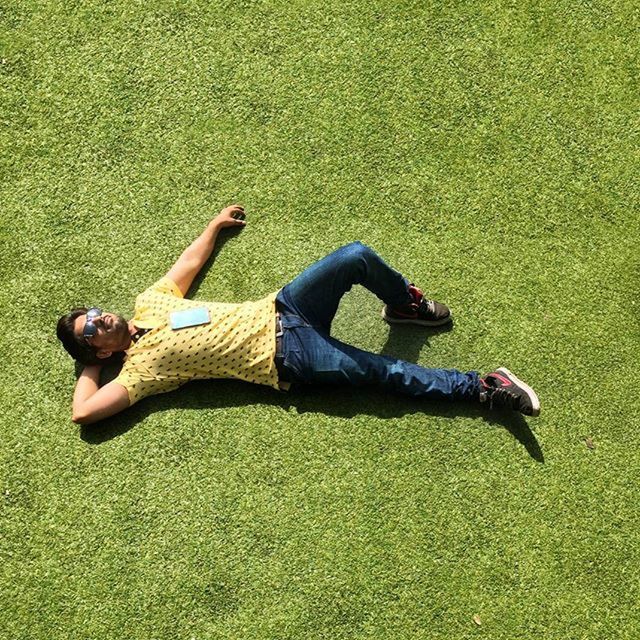 low section, person, lifestyles, shoe, leisure activity, high angle view, grass, sitting, relaxation, footwear, casual clothing, lying down, jeans, green color, day, personal perspective