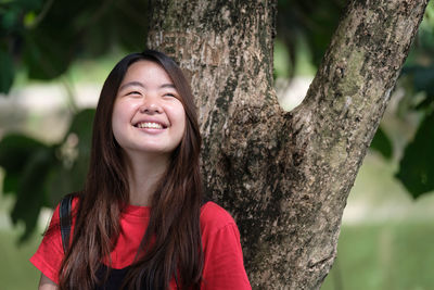 Portrait of smiling young woman against tree trunk