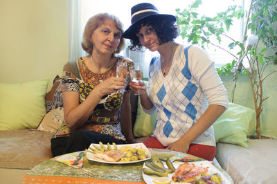 Portrait of friends toasting drinks while sitting on sofa at home