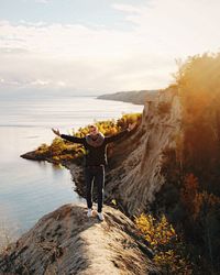 Rear view of man standing on rock by sea against sky