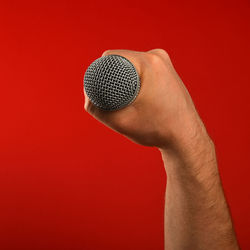 Close-up of cropped hand holding microphone against red background
