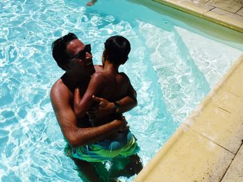 High angle view of shirtless father and son embracing in pool
