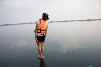 Rear view of man standing on lake against sky