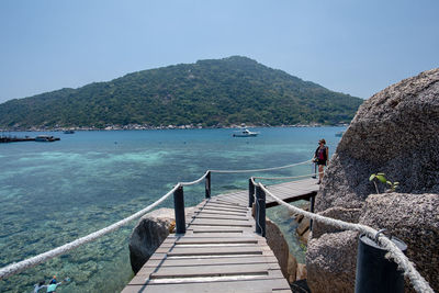 Pier amidst sea and mountains against clear sky