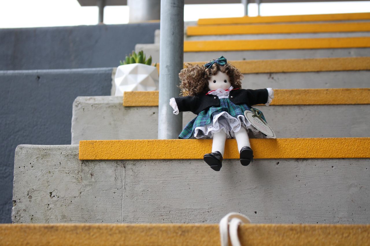 yellow, staircase, childhood, one person, architecture, child, sitting, full length, blue, day, casual clothing, wall, women, steps and staircases, lifestyles, built structure, emotion, outdoors, toy, front view, leisure activity, fun, happiness, female, cute, person, clothing, smiling