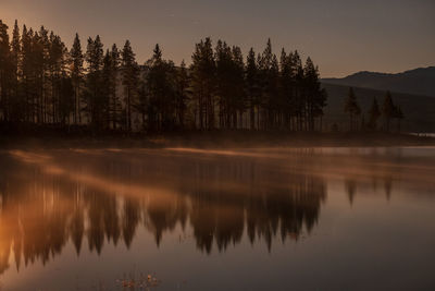 Reflection of trees in lake against sky during moonrise 