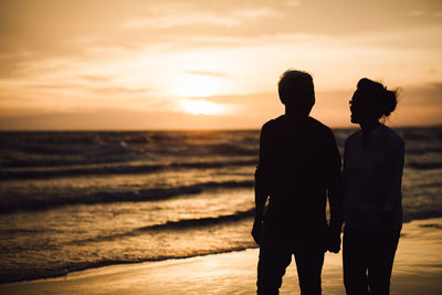 Friends standing on beach against sky during sunset