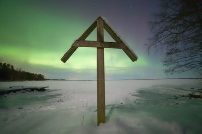 Wooden structure on snow covered field against aurora borealis at night