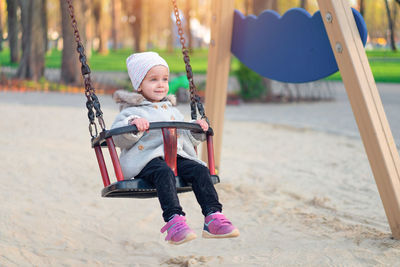 Smiling girl looking away while sitting on swing at playground