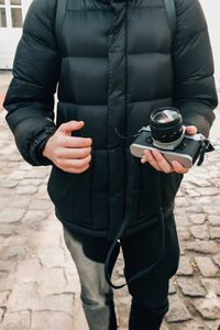 Midsection of man holding camera while standing outdoors