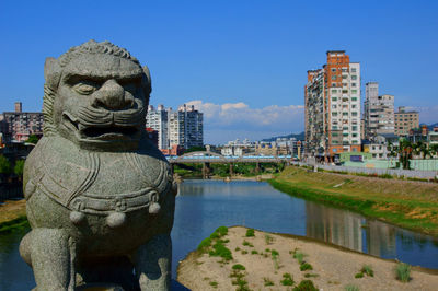 Statue by river against buildings in city against sky