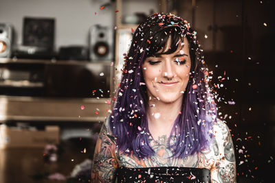 Smiling young woman with colorful confetti standing at home