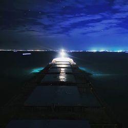 Illuminated lights by sea against sky at night