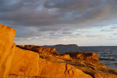 Rock formations by sea against sky during sunset