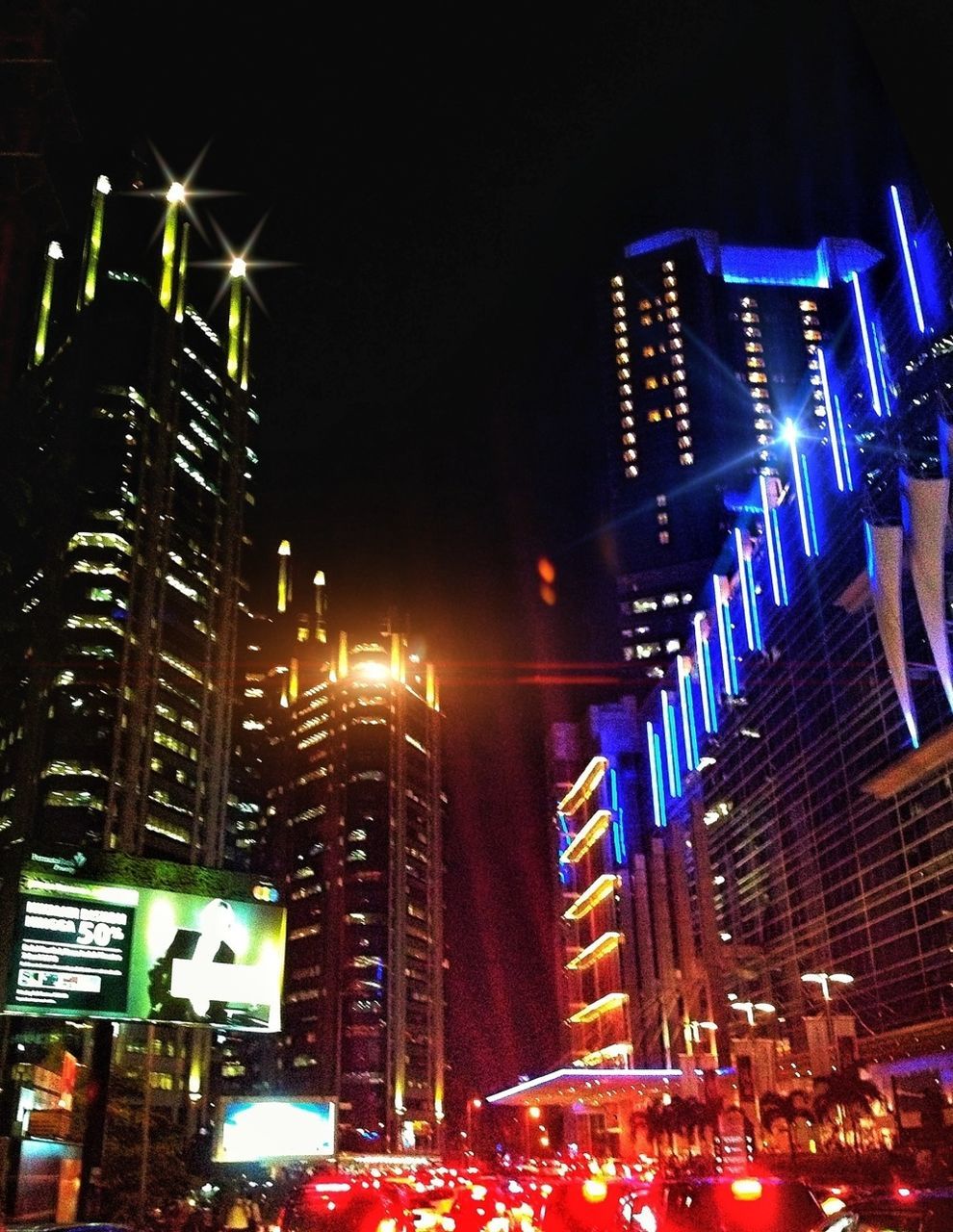 illuminated, night, building exterior, architecture, city, built structure, skyscraper, tall - high, modern, low angle view, office building, street light, street, city life, lighting equipment, city street, tower, traffic, car, building