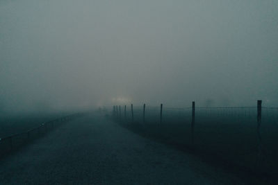 Fence on landscape against sky during foggy weather