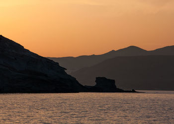 Scenic view of sea and silhouette mountains against orange sky