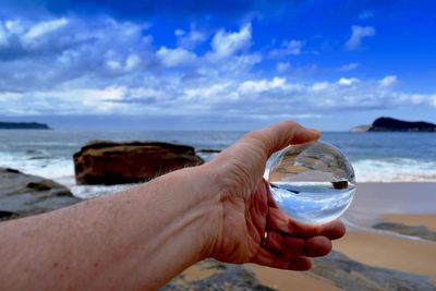 Midsection of person holding sunglasses at beach against sky