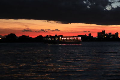 Silhouette city by river against sky during sunset