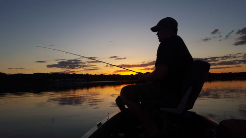 Side view of silhouette man fishing in lake against sky during sunset