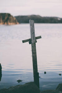 Cross on wooden post in sea against sky