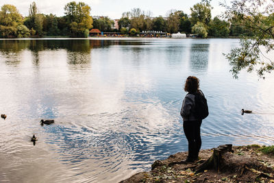 Rear view of woman standing by lake against sky