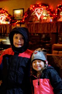 Smiling cute siblings standing against illuminated christmas lights at home