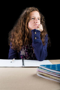 Young woman studying at desk against black background