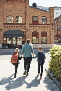 Rear view of woman taking sons to school while walking on footpath