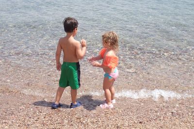 Full length of siblings standing on shore at beach