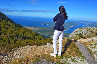 Rear view of woman standing on mountain while looking at sea 