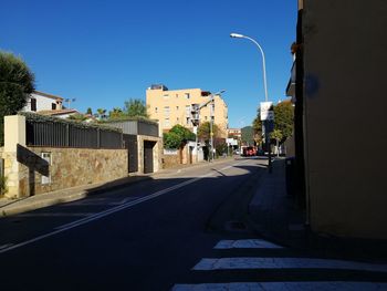 Road amidst buildings against clear blue sky