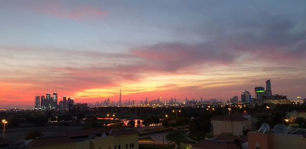 Illuminated buildings in city against sky during sunset