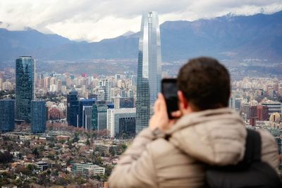 Rear view of man photographing cityscape against sky