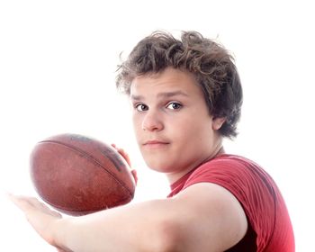 Portrait of teenage boy holding ball against white background