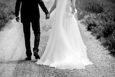Rear view low section of wedding couple walking on gravel road