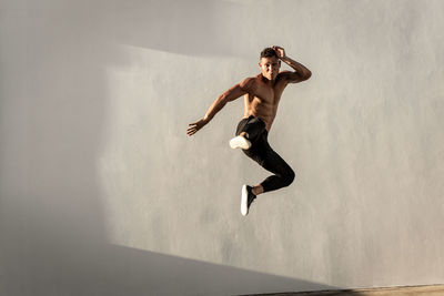 Full length of shirtless man jumping against wall